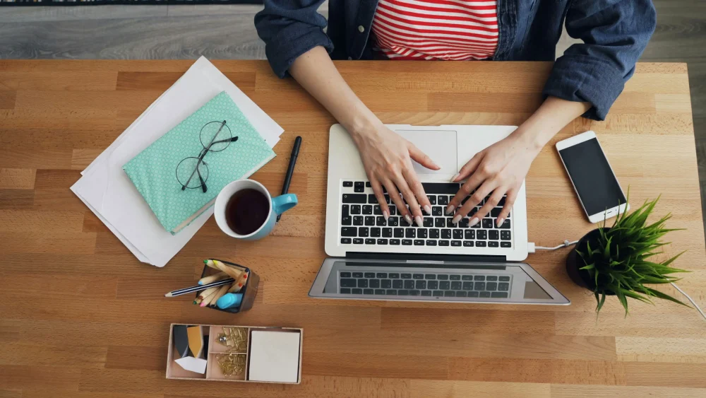 top view of woman using laptop typing in office at wooden desk