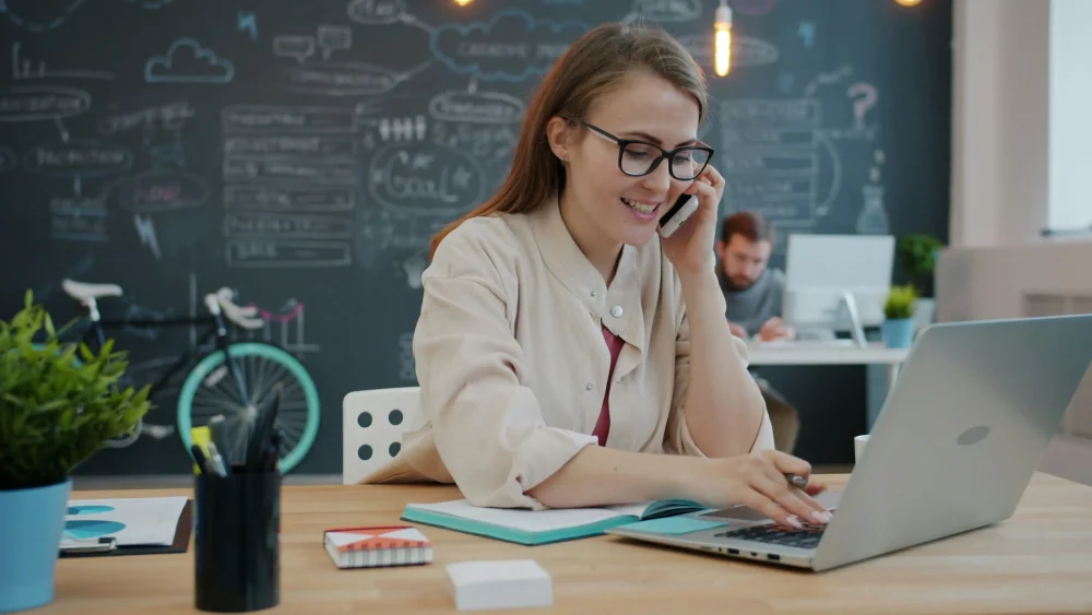 Woman talking on phone at desk with laptop